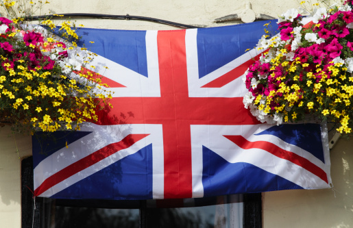 Union Jack flag with hanging basket displays. A patriotic display over the door to a public house in Surrey, England. This is July 2012, in the midst of the celebrations for the Diamond Jubilee of Queen Elizabeth II. The UK flag consists of three elements: the cross of St. George (red on white) for England, the cross of St. Andrew (white diagonal on blue) for Scotland, and the 'cross of St. Patrick' (red diagonal on white) for Ireland. The original Union Jack / Union Flag, adopted in 1606, was symmetrical. The red cross of St. George was outlined in white overlaid on top of a St. Andrew's flag, which was blue with a white X. In 1801, an Act of Union which made Ireland a co-equal member of the United Kingdom made it necessary to add a symbol for Ireland to the flag.