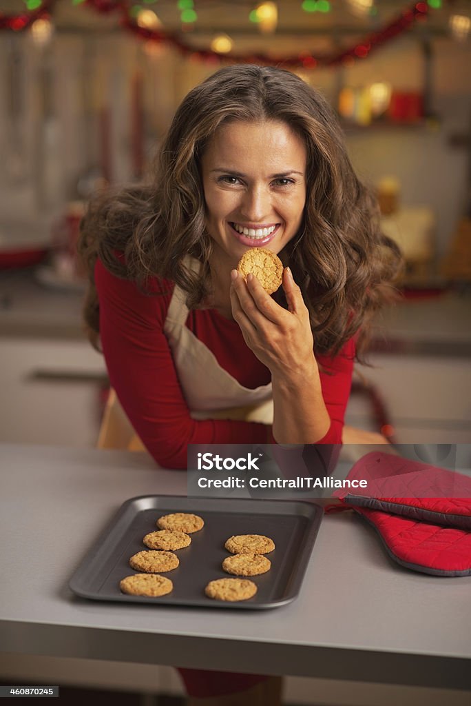 Happy young housewife eating christmas cookie in kitchen Adult Stock Photo