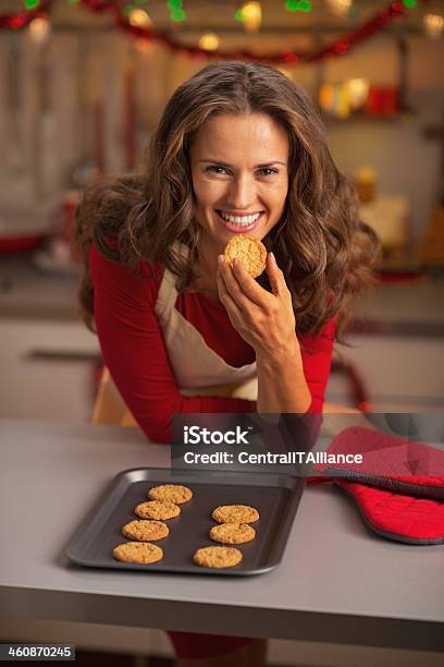 Happy Young Housewife Eating Christmas Cookie In Kitchen Stock Photo - Download Image Now