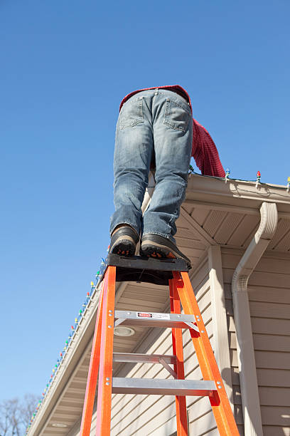 istock Man Installing Christmas Lights Stands on Ladder Top 460871547