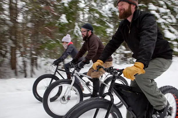 Two men and a woman are riding their snow bikes on a groomed trail in northern Idaho. Shot at a slow shutter speed while panning to accentuate motion and blur.