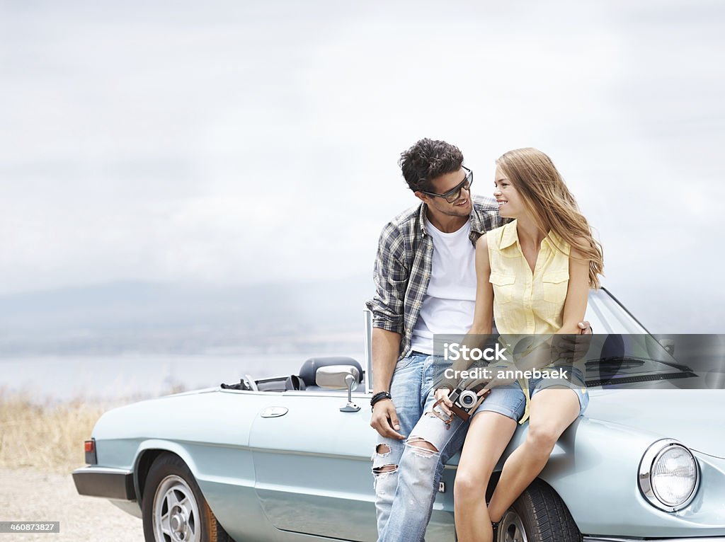 Are you enjoying the trip? Attractive young couple sitting on the hood of their convertible while out on a roadtrip 20-24 Years Stock Photo