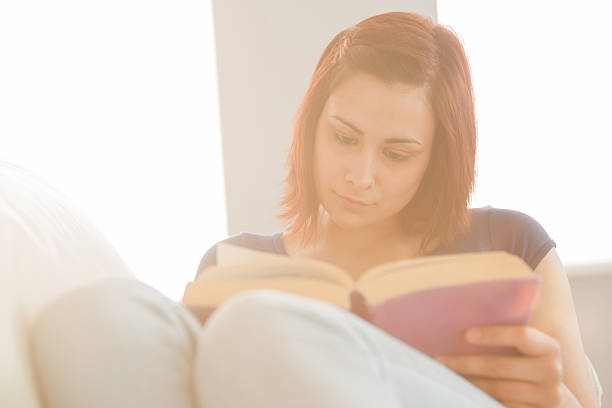 istock Content woman sitting on her couch reading a book 460883561