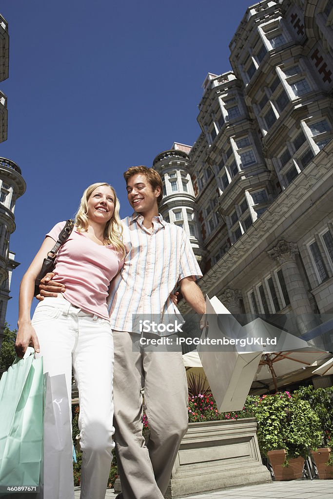 Couple On City Street With Shopping Bags Low angle view of young couple walking down city street with shopping bags Adult Stock Photo
