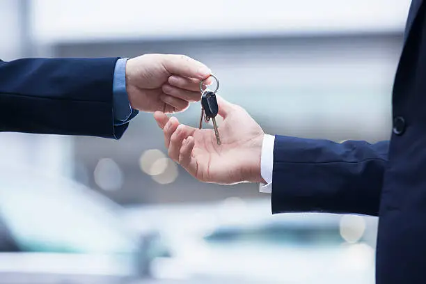 Photo of Salesman handing over keys for new car to young businessman