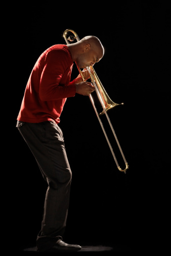 Side view of an African American man playing the trombone against black background