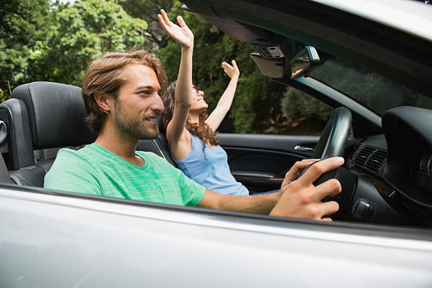 istock Cool couple driving a silver convertible with woman cheering 460946831