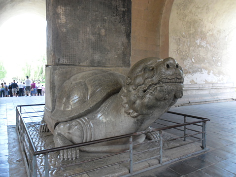 Beijing, China - May 24, 2012: A view of Ming Dynasty Tombs, Beijing, China. A turtle statue at Ming Dynasty Tombs. Tourists and locals are at the Tombs’s area. The site of the Tombs is chosen according to Feng Shui (Geomancy). Some Chinese Emperors are buried in this area. It is listed as a UNESCO World Heritage Site.