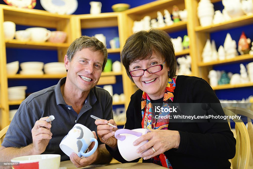 Happy Retired Couple Painting Pottery Mature adults painting pottery together.  They are in a pottery workshop.    Painting - Activity Stock Photo