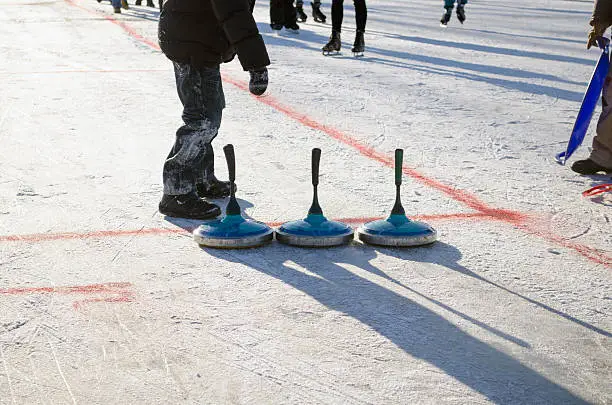 people play winter game curling eisstock and slide skate playground on frozen lake ice.