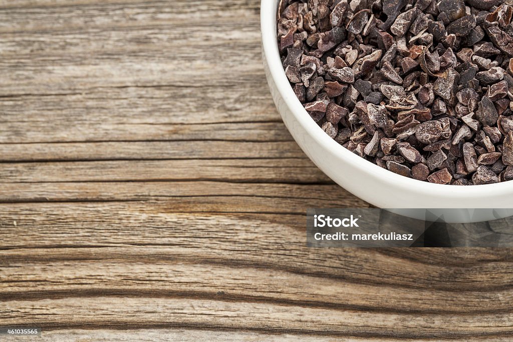 Raw cacao nibs Raw cacao nibs in a small ceramic bowl against grained wooden background Antioxidant Stock Photo