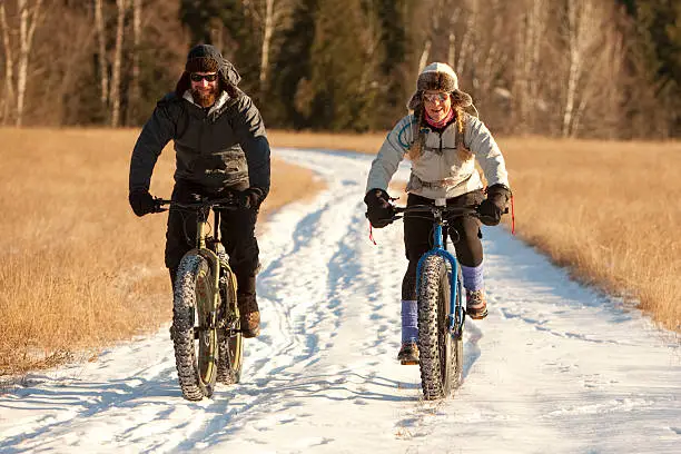 A man and a woman are riding fatbikes on a snow covered trail on a bright sunny day in northern Idaho.
