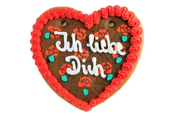 gingerbread heart cookie with German words "Ich liebe dich" (engl. I love you) in red and white. On background roses of icing. Typical Beer Fest or Valentines day gift on white background.