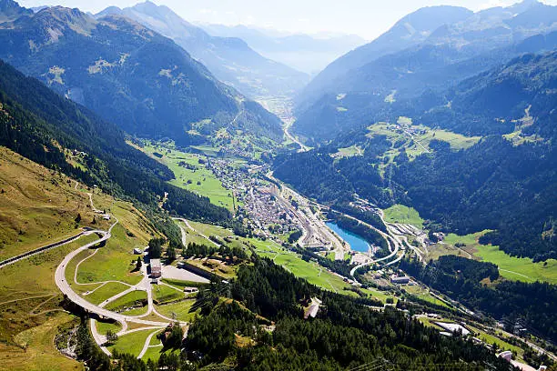 Aerial view down to Airolo from St. Gottard pass street. Old pass street is winding uphill at left side. In valley is passing highway.