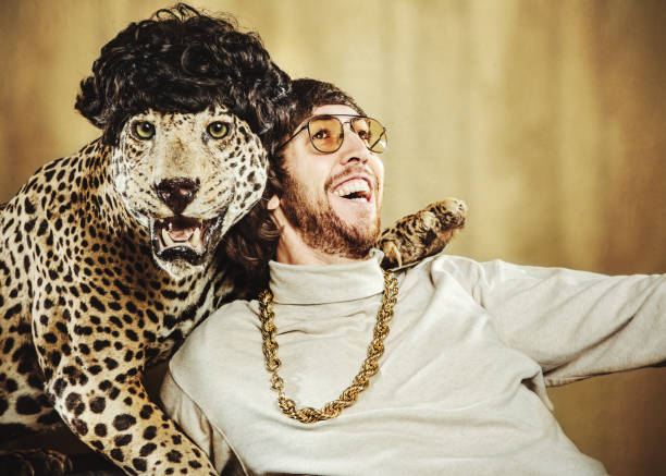Retro Man Poses with Wig Wearing Leopard Best friends; a man with shaggy hair and 1970's style relaxes with a leopard wearing a wig, their arms around each other. The man smiles, and it looks like the leopard does too. Horizontal image. taxidermy cat stock pictures, royalty-free photos & images