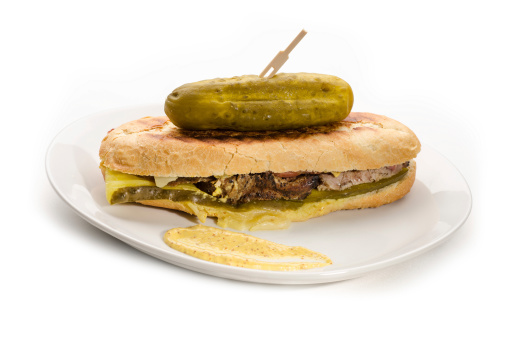 Cuban sandwich on a plate with a pickle. Sandwich photographed on with background.