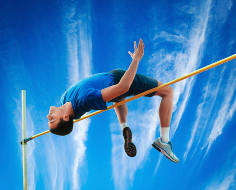 High jumper over hurdle against beautiful sky with vertical clouds.