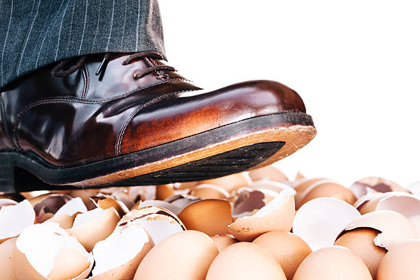 Businessman's shoes walking on eggshells Walking on eggshells metaphor showing close-up of male human lower leg above broken eggshells, with copy space isolated on white. animal egg walking on eggshells walking broken stock pictures, royalty-free photos & images