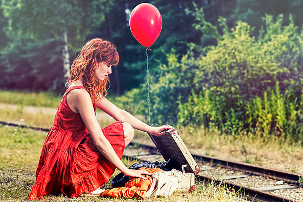 Summer portrait of a romantic girl outdoors with big fluffy dandelions. A 13-year-old girl with a guitar is lonely, and sits sadly on the rails. The desire and inability to travel.