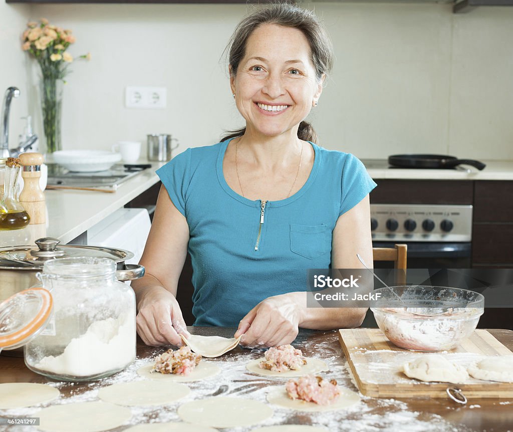 Smiling mature woman making meat dumplings Smiling mature woman making meat dumplings (pelmeni)  at domestic kitchen Cooking Stock Photo