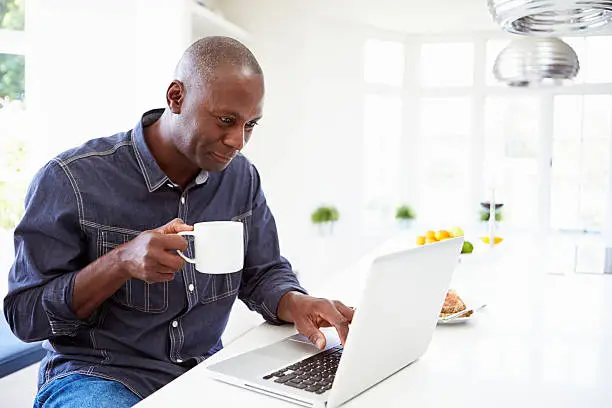 Photo of An African American man using his laptop while drinking