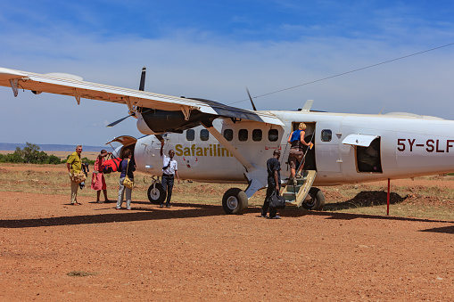 Masai Mara, Kenya - March 05,2011: Passengers boarding small turbo-prop aircraft at Olkiombo Airstrip on the Masai Mara; a Masai tribesman is seen loading baggage, and a couple of passengers making sure their bags are loaded.  The whole process is informal and as rustic as the airstrip. Tourists fly in and out of the great Rift Valley on these small turbo-props. It is very often the beginning, or the end of their East African Kenyan Safari.