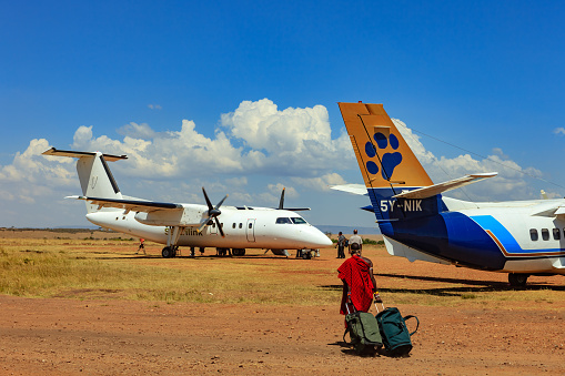 Masai Mara, Kenya - March 05,2011: Boarding small turbo-prop aircraft at Olkiombo Airstrip on the Masai Mara; a Masai tribesman wheels two pieces of baggage to load on to the airplane.  Some passengers are seen moving towards the aircraft.