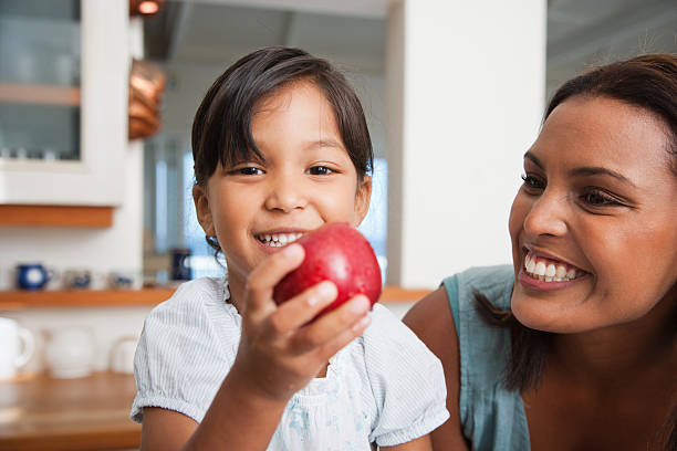 母娘のキッチンを持つレッドアップル添え - child eating apple fruit ストックフォトと画像