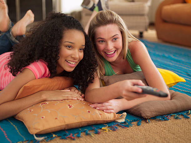 Two teenage girls lying down watching television with remote control smiling  teenagers only photos stock pictures, royalty-free photos & images