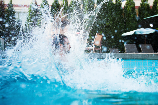 Young man jumping into a pool with water splashing all around him
