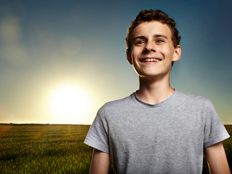 Closeup of a teenage boy with the sun behind him at sunset, in a wheat field
