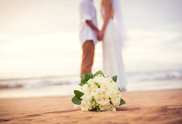 recién casados pareja sosteniendo las manos en la playa - boda playa fotografías e imágenes de stock