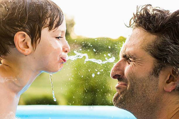 Water fight Young boy spits water playfully into dad's face. spit stock pictures, royalty-free photos & images