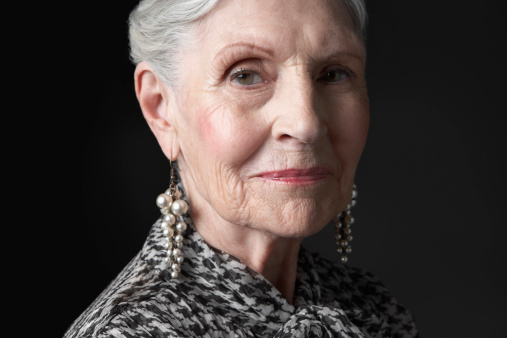 Closeup portrait of a senior woman with pearl earrings against black background