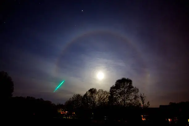 This a photo of a meteorite and a Moonbow around a Hunter's Moon. A moonbow is technically known as a 22º moon halo. The 22º Moon Halo is formed when moonlight passes through ice crystals in the atmosphere and are refracted approximately 22º.