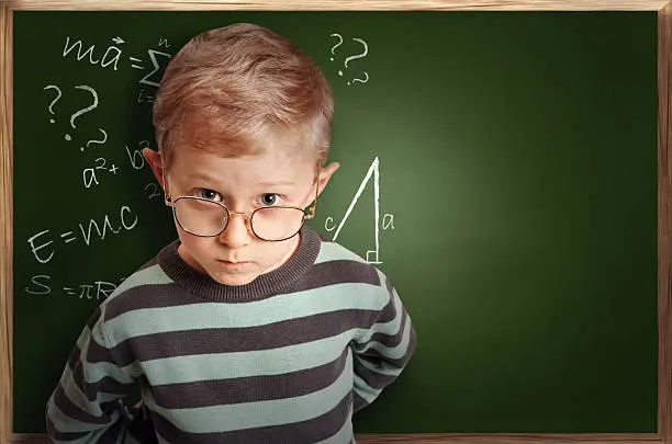 Clever pupil boy in eyeglasses near schoolboard