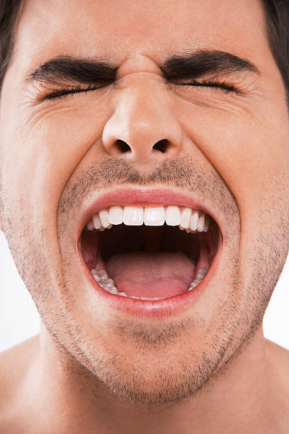 Closeup of young man screaming with eyes closed on white background