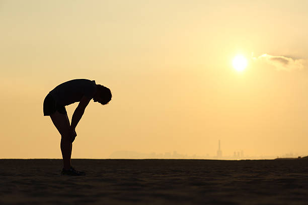 silhouette der ein erschöpfter sportler bei sonnenuntergang - müde stock-fotos und bilder