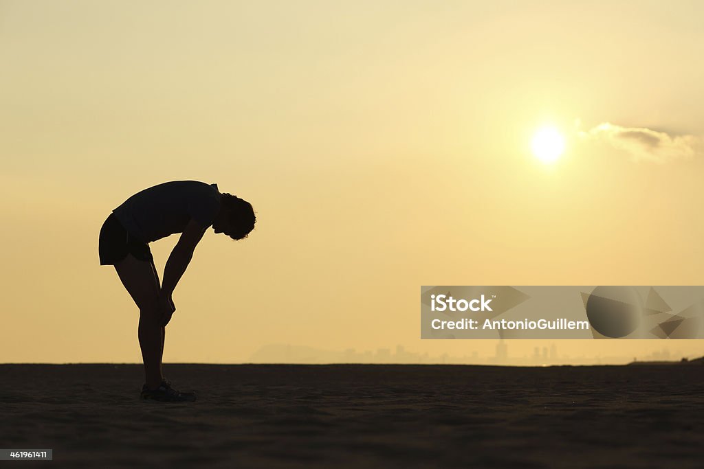 Silueta de un deportista agotado en puesta - Foto de stock de Agotamiento libre de derechos