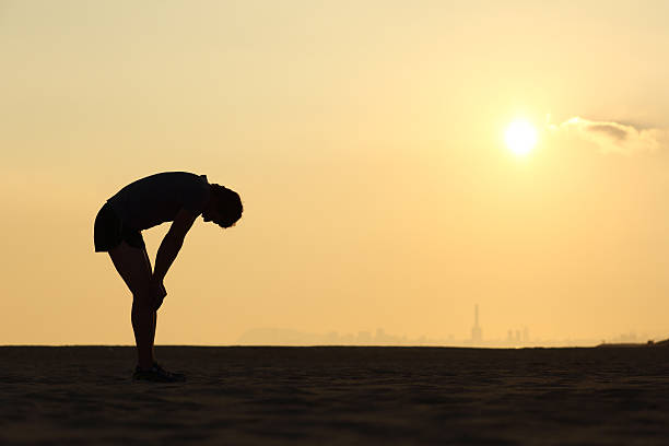 silhouette d'un sportif épuisé au coucher du soleil - fatigue photos et images de collection