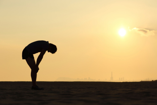 Silhouette of an exhausted sportsman at sunset with the horizon in the background