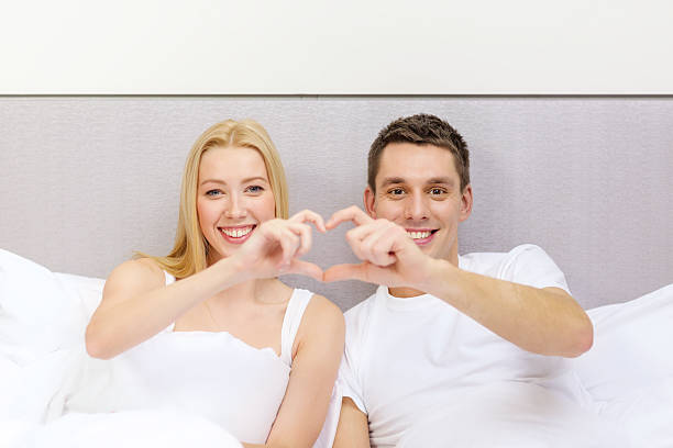 istock smiling couple showing heart symbol in bed 461963185