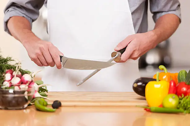 Professional chef sharpening knife including assorted fresh vegetables