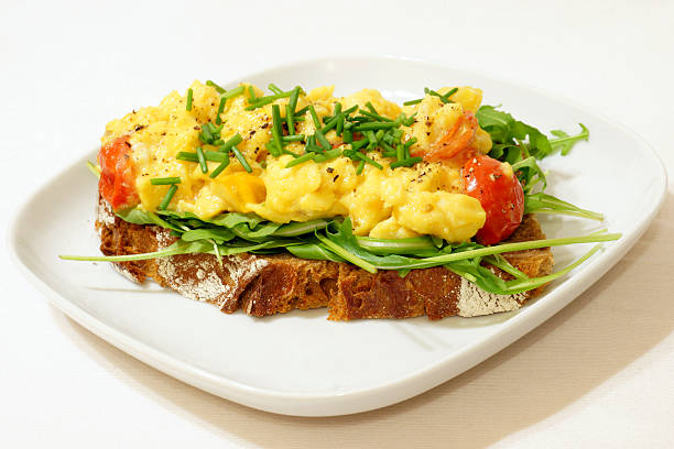 Scrambled Eggs on Rye Bread A healthy breakfast of scrambled eggs on rye bread with arugula salad and cherry tomatoes. egg cherry tomato rye stock pictures, royalty-free photos & images