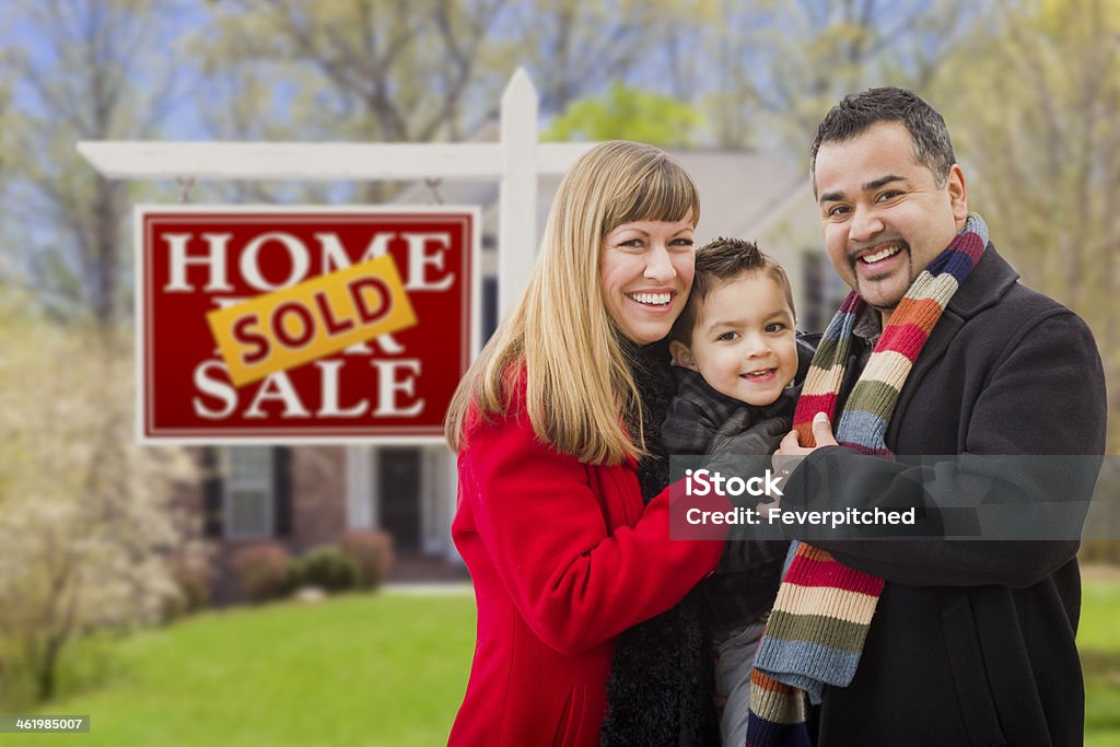 Family in Front of Sold Real Estate Sign and House Warmly Dressed Young Mixed Race Family in Front of Sold Home For Sale Real Estate Sign and House. 30-39 Years Stock Photo