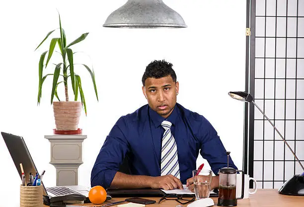 An image of an Indian office worker with a blue shirt behind his desk