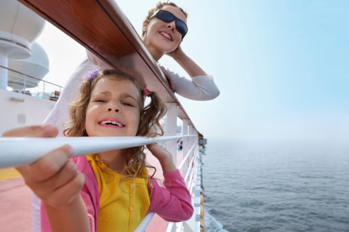 Smiling mother and daughter traveling on big cruise ship, other ship in sea
