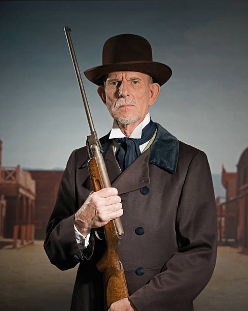 senior western-mann mit braunen mantel und mütze hält gewehr. - wild west audio stock-fotos und bilder