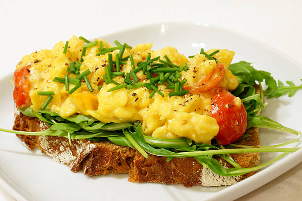 Scrambled Eggs on Rye Bread A healthy breakfast of scrambled eggs on rye bread with cherry tomatoes and arugula salad. egg cherry tomato rye stock pictures, royalty-free photos & images