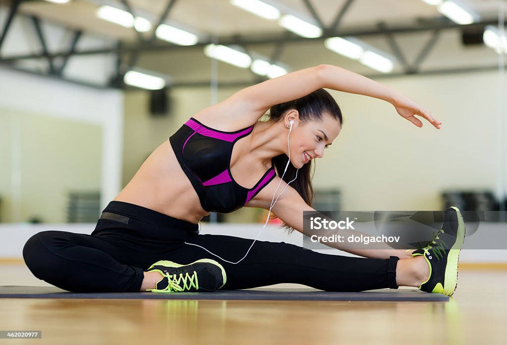 Estiramiento mujer joven con auriculares en el gimnasio - Foto de stock de Actividades y técnicas de relajación libre de derechos